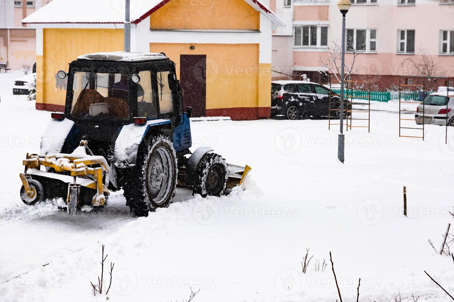 The tractor clears the road from snow in winter during a snowfall. photo