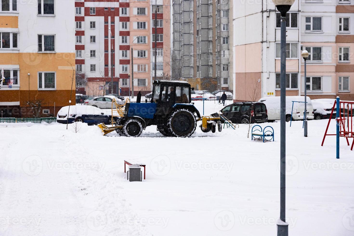 The tractor clears the road from snow in winter during a snowfall. photo