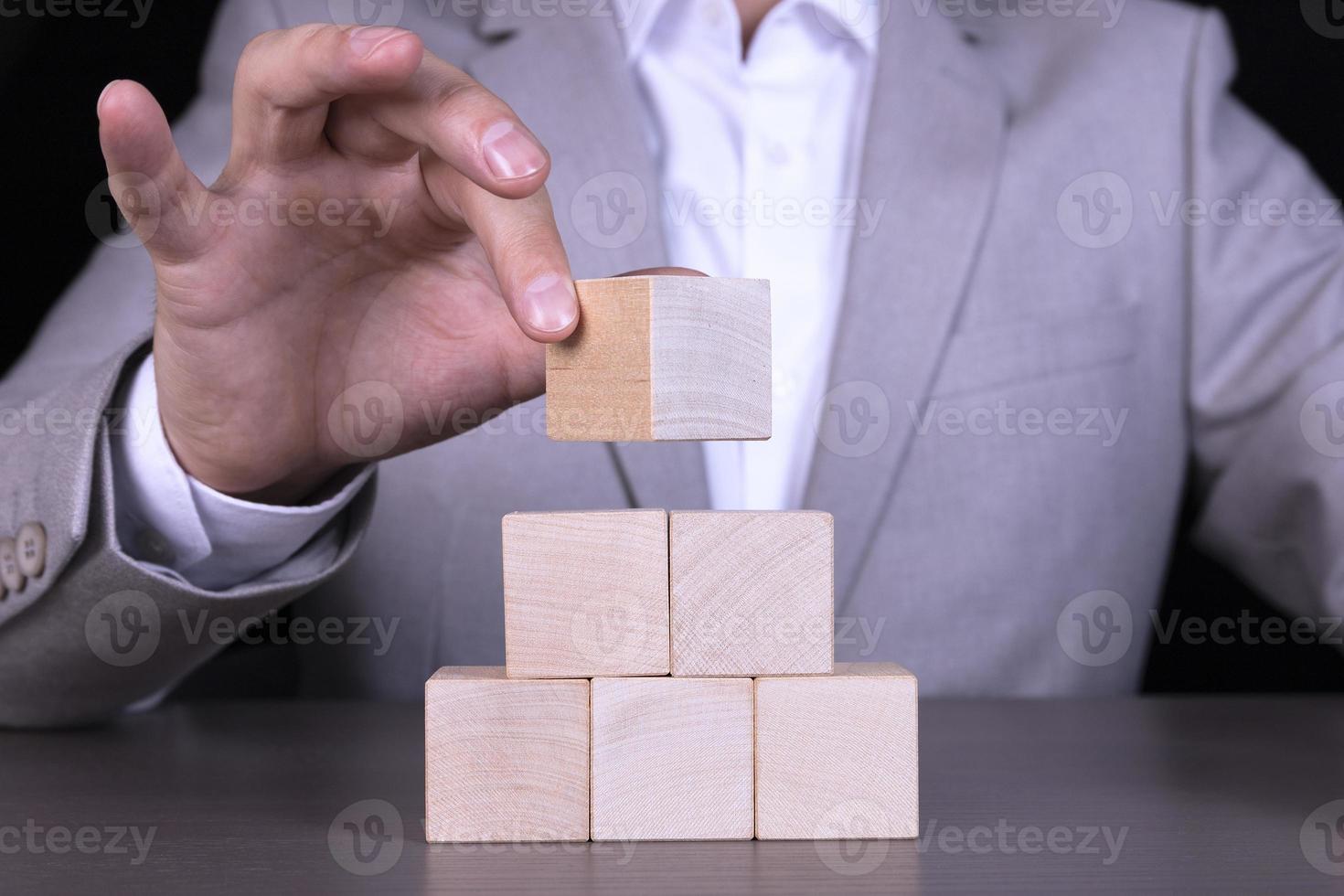 Businessman stacking wood cube blocks in pyramid with blank copy space for icons photo