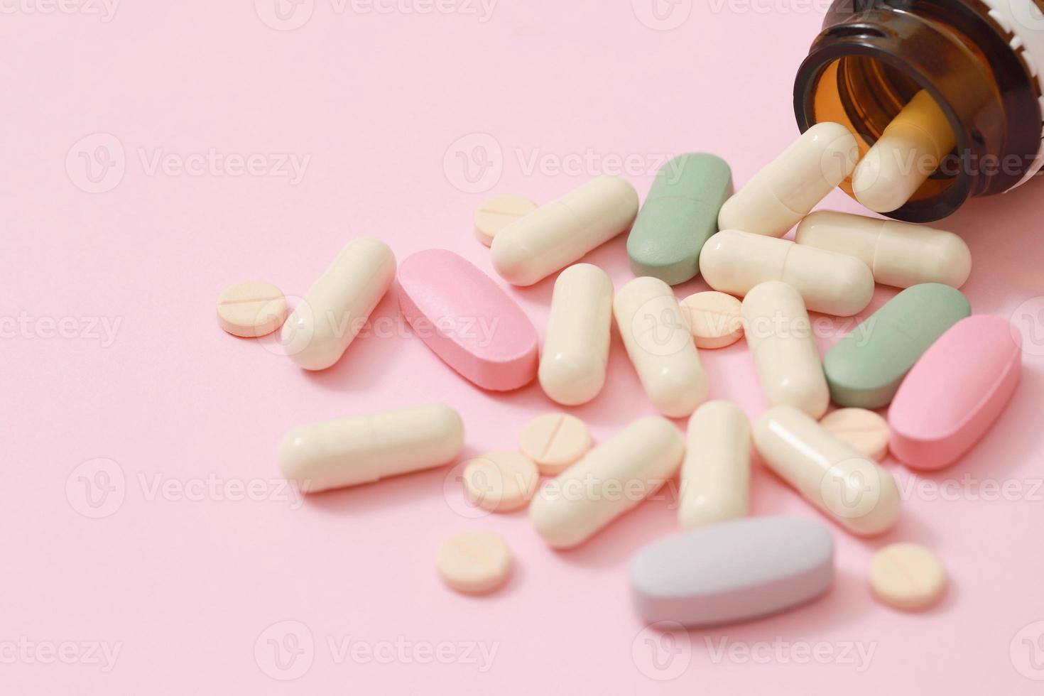 bote de pastillas derramándose. Cápsula de píldoras de colores sobre tabletas de superficie sobre fondo rosa. concepto de farmacia de atención médica de medicamentos. productos farmacéuticos antibióticos píldoras medicina en blisters. foto