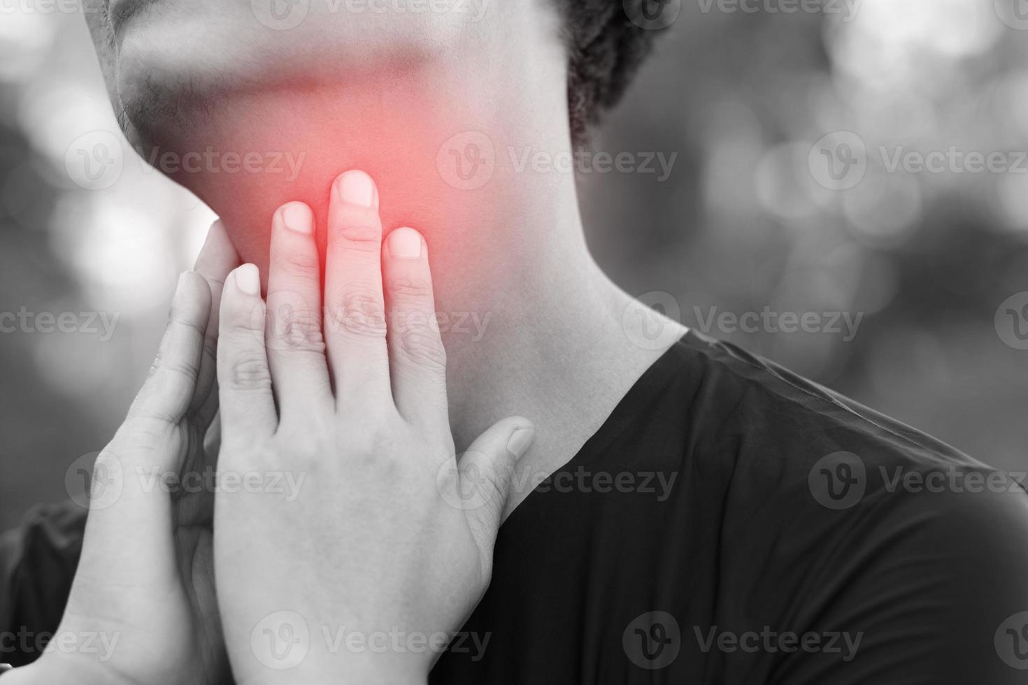 sore throat pain. Closeup of young man sick holding her inflamed throat using hands to touch the ill neck in blue shirt on gray background. Medical and healthcare concept. Focus red on to show pain. photo
