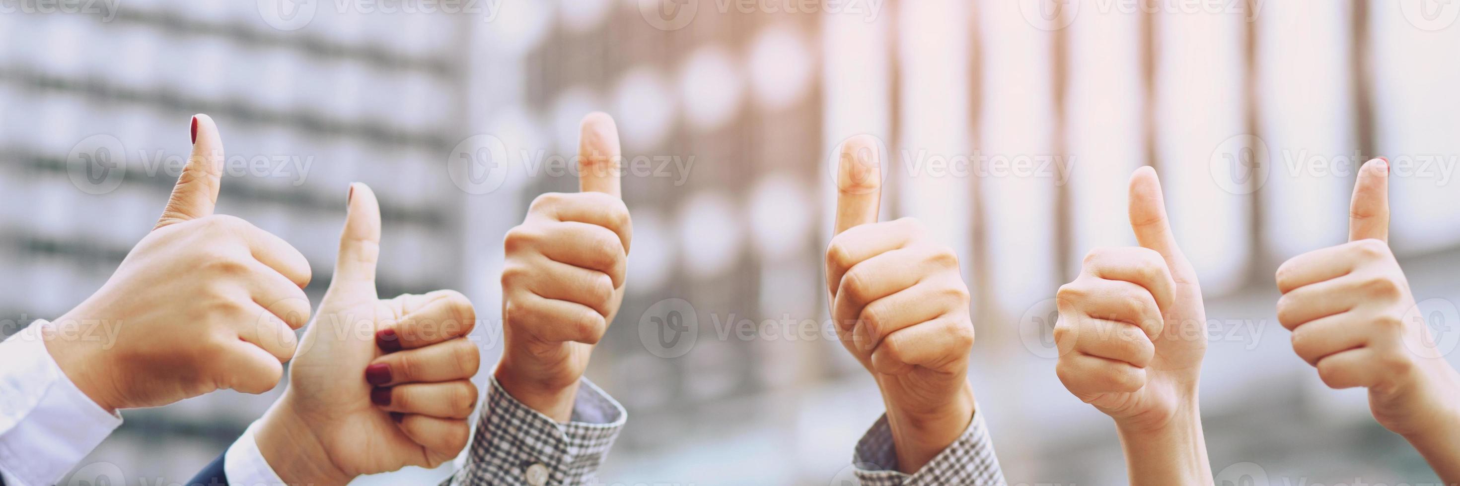 Happy cheerful Group of business people raising arms over thumb up office background successful entrepreneurs.  Success team achieving goals. photo