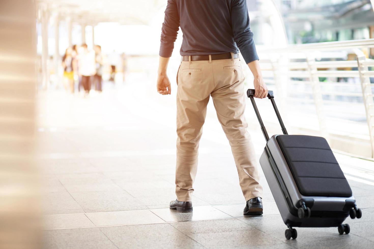 empresario caminando fuera del edificio de transporte público con equipaje en hora punta. viajero de negocios tirando de la maleta en la moderna terminal del aeropuerto. viaje de negocios de equipaje. foto