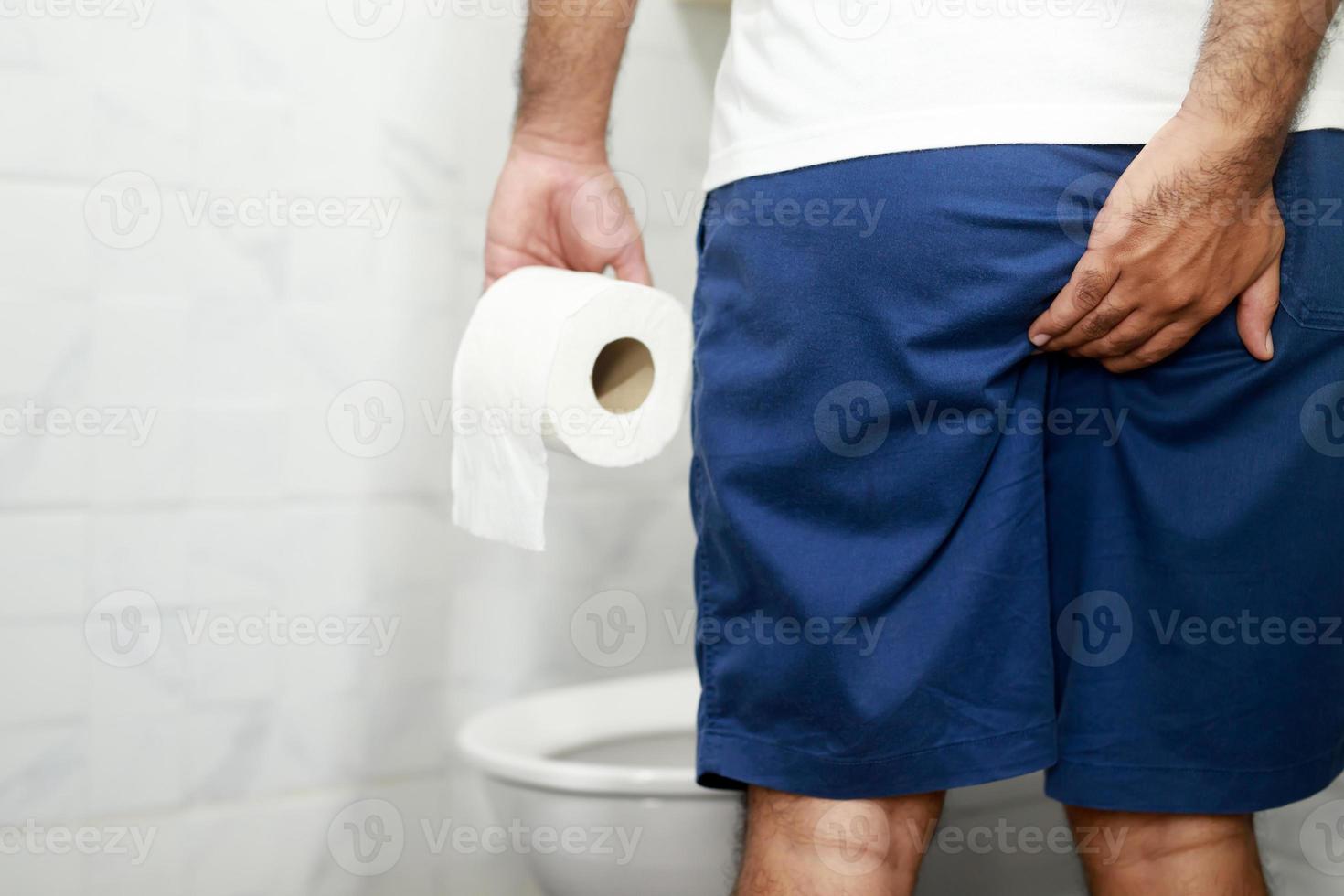 Man suffers from diarrhea hand hold tissue paper roll in front of toilet bowl. constipation in bathroom. Treatment stomach pain and Hygiene, health care photo