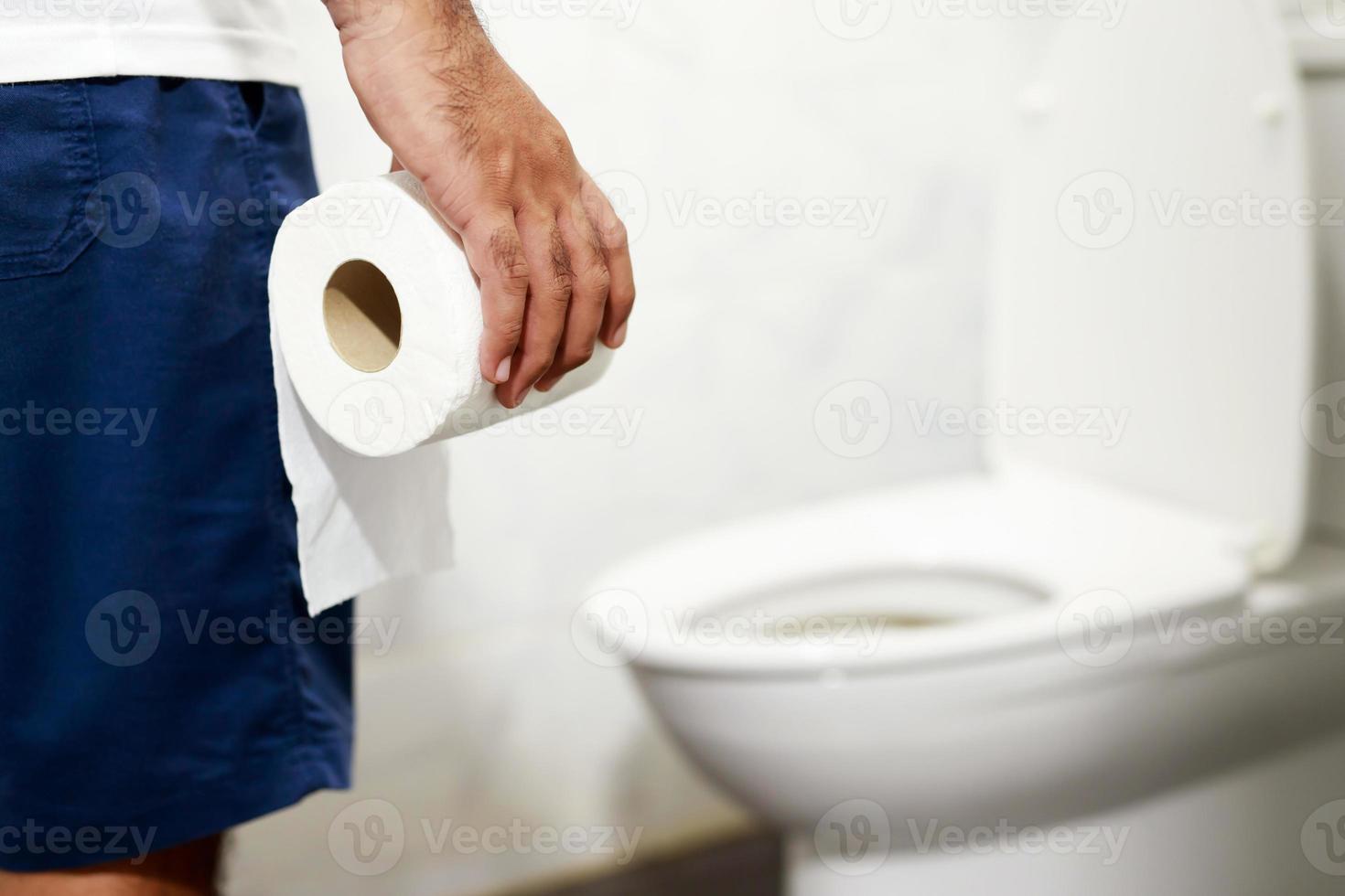 Man suffers from diarrhea hand hold tissue paper roll in front of toilet bowl. constipation in bathroom. Treatment stomach pain and Hygiene, health care photo