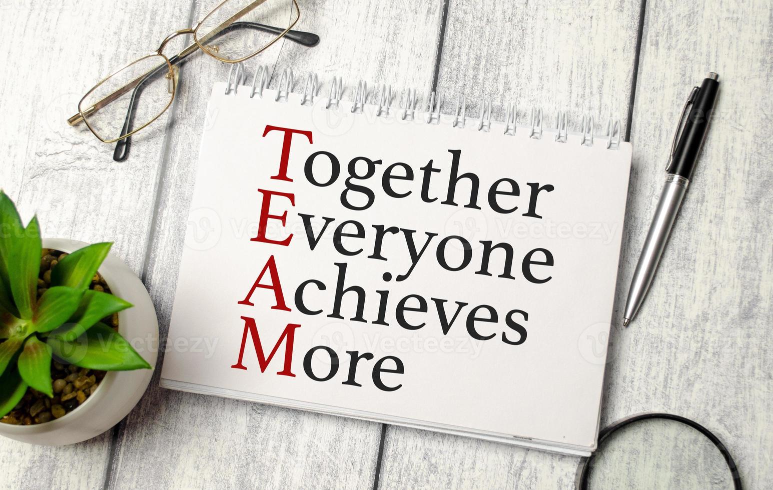 together everyone achieves more words and calculator, pen and glasses on wooden background photo