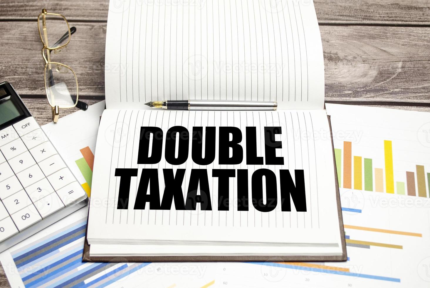 DOUBLE TAXATION text on notepad and calculator with charts photo