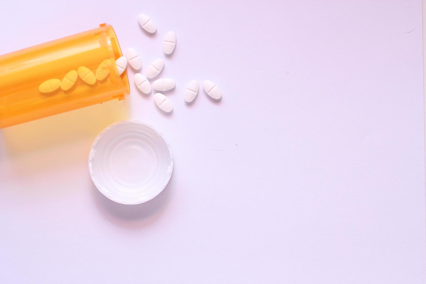 Oval pills and orange pill bottles were spread out on the white tabletop. photo