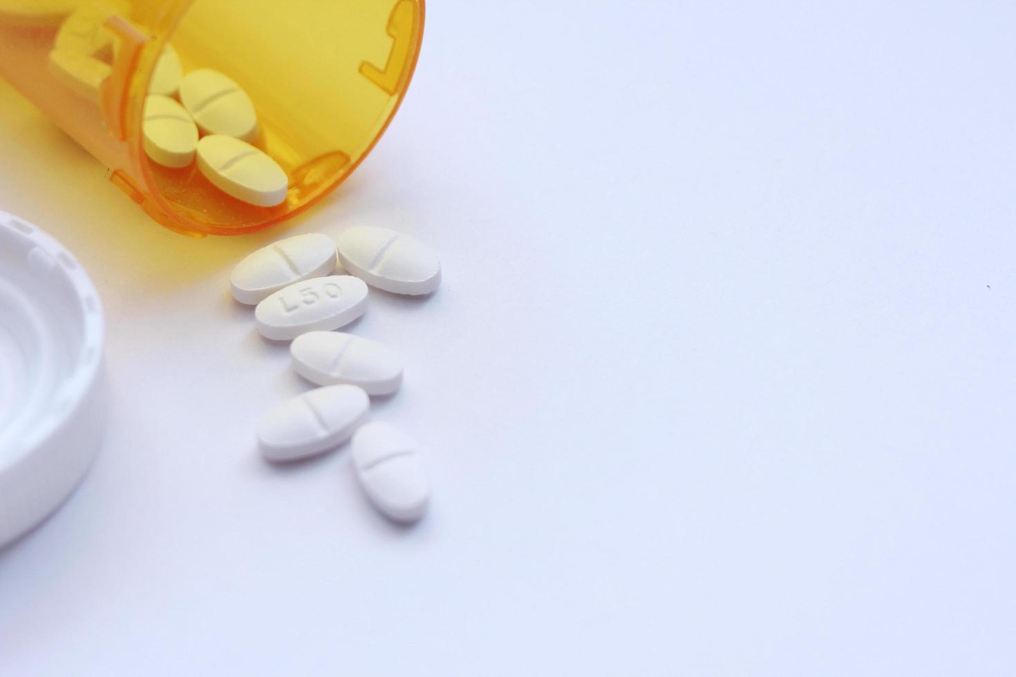 Oval pills and orange pill bottles were spread out on the white tabletop. photo