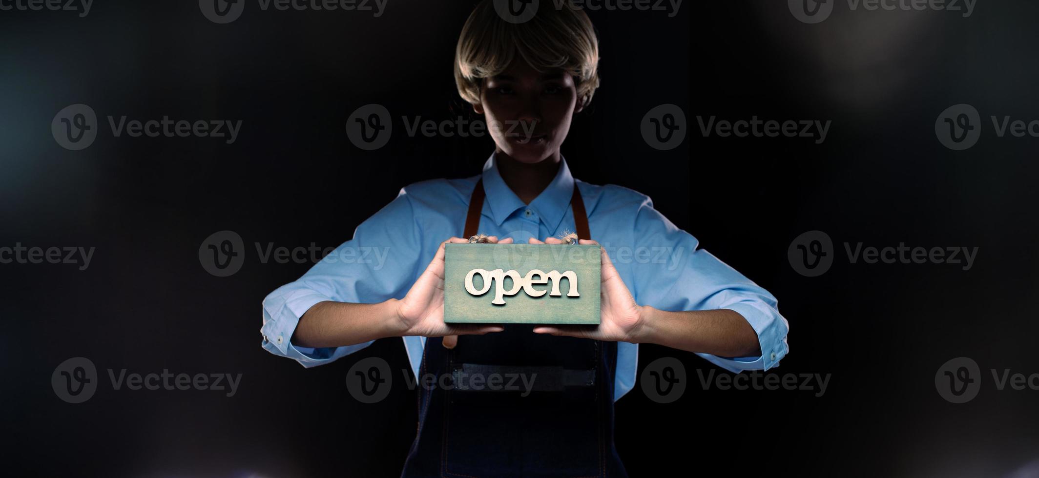 Caucasian person hold Open Sign Business to show service at door entrance store, cafe, retail and welcome shop. Happy Entrepreneur female blonde hair wear waitress dress as open business time concept photo