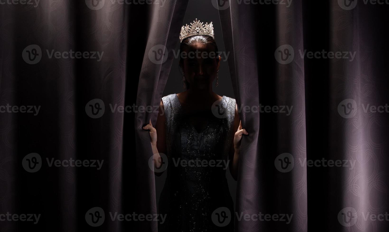 el concurso de belleza miss pageant viste un vestido largo de noche de lentejuelas con una corona de diamantes brillantes, una mujer asiática abre una cortina morada después de ganar la ronda final como una nueva forma de vida, oportunidad, cambio, aislada foto