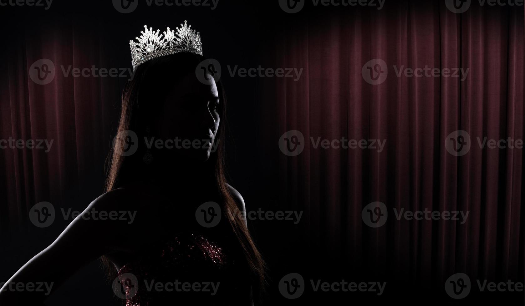 Portrait of Miss Pageant Beauty Contest in sequin Evening Ball Gown long dress with sparkle light Diamond Crown, silhouette low key exposure with curtain, studio lighting dark background dramatic photo