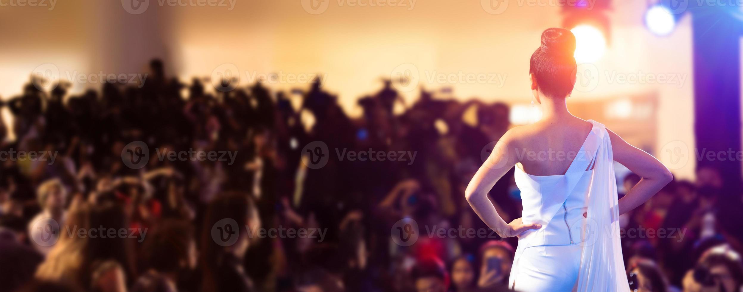 Woman stand in front of Media Press Television camera as Model Fashion Show or Miss Beauty queen pageant contest to empower people, Light to back view of unrecognizable woman photo