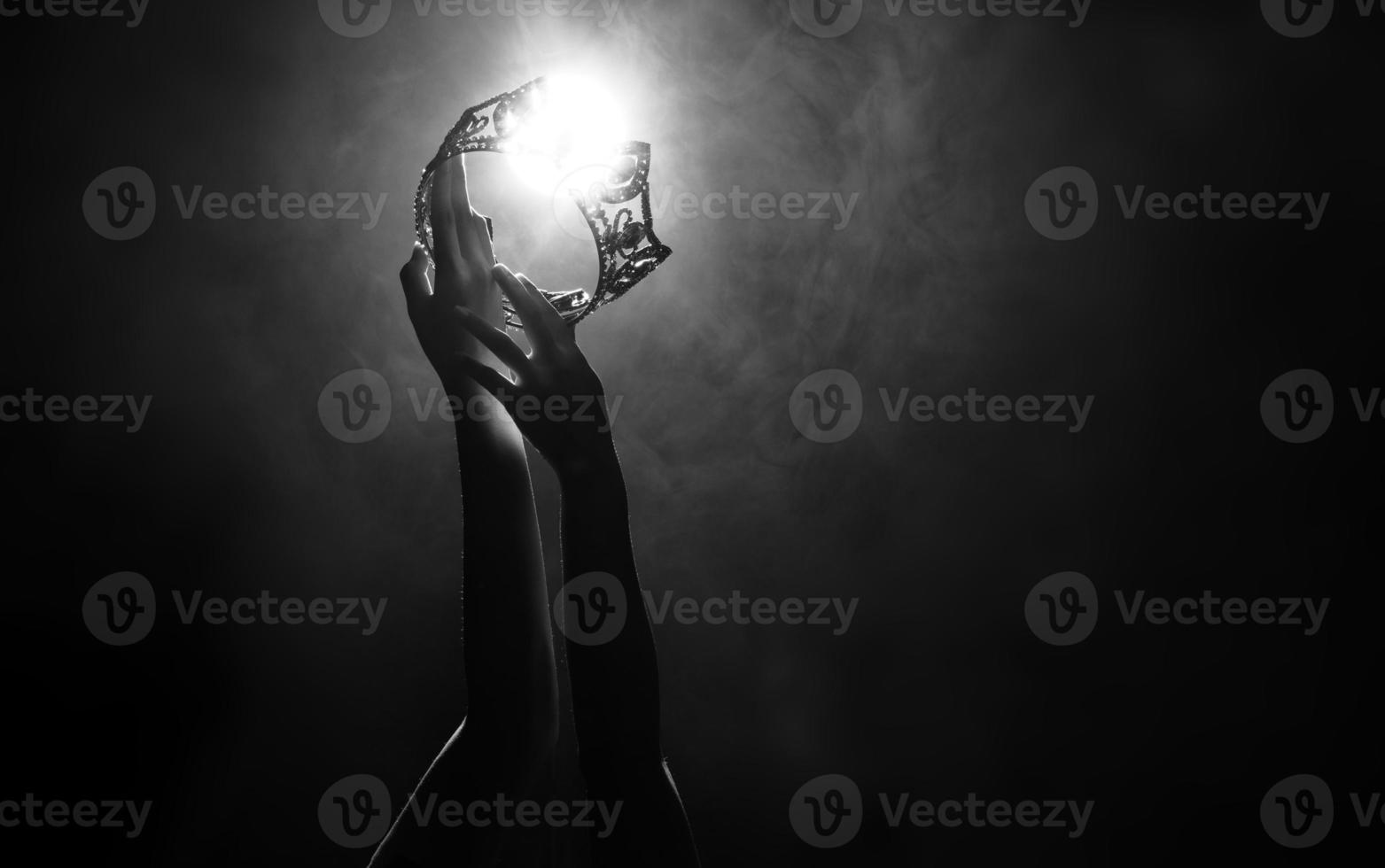 Silhouette abstract of two hands try to reach Diamond Crown as Miss Beauty Queen Pageant Contest as final competition, finale winner moment. Backlit smoke low exposure dark background copy space photo