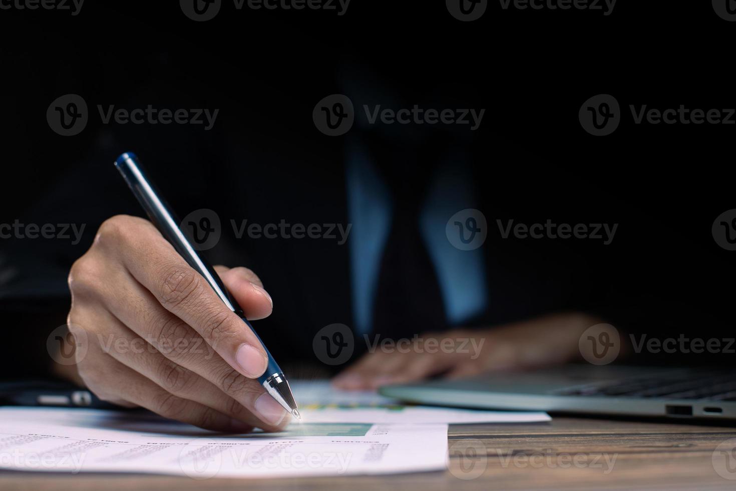 Businessman executive manager hand point pen to paper business document, graph sales growth, partnership agreement and working on desk in night time at office, close up photo