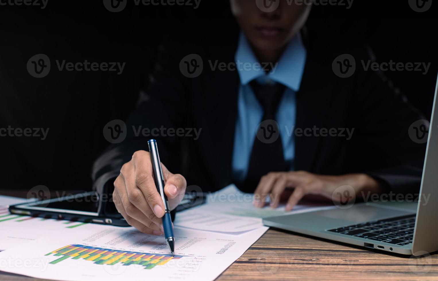 Businessman executive manager hand point pen to paper business document, graph sales growth, partnership agreement and working on desk in night time at office, close up photo