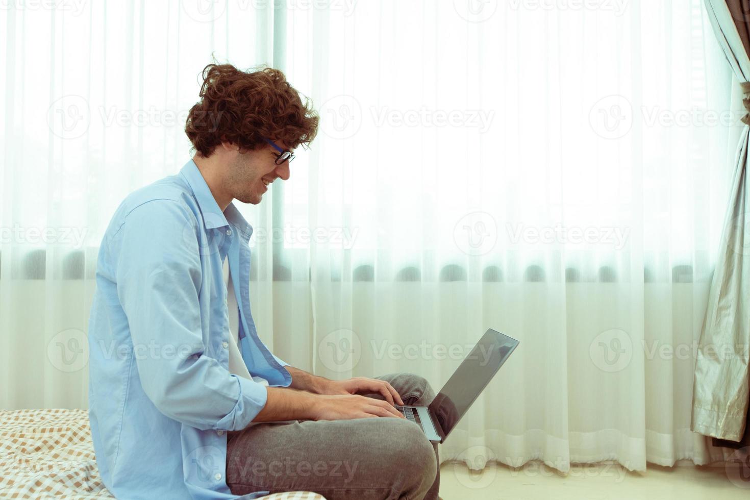 Young Caucasian Man work from home on laptop and connect online to office indoor for remote internet workplace. Young Adult male  is freelance work smart on notebook sitting on Bed bedroom, copy space photo