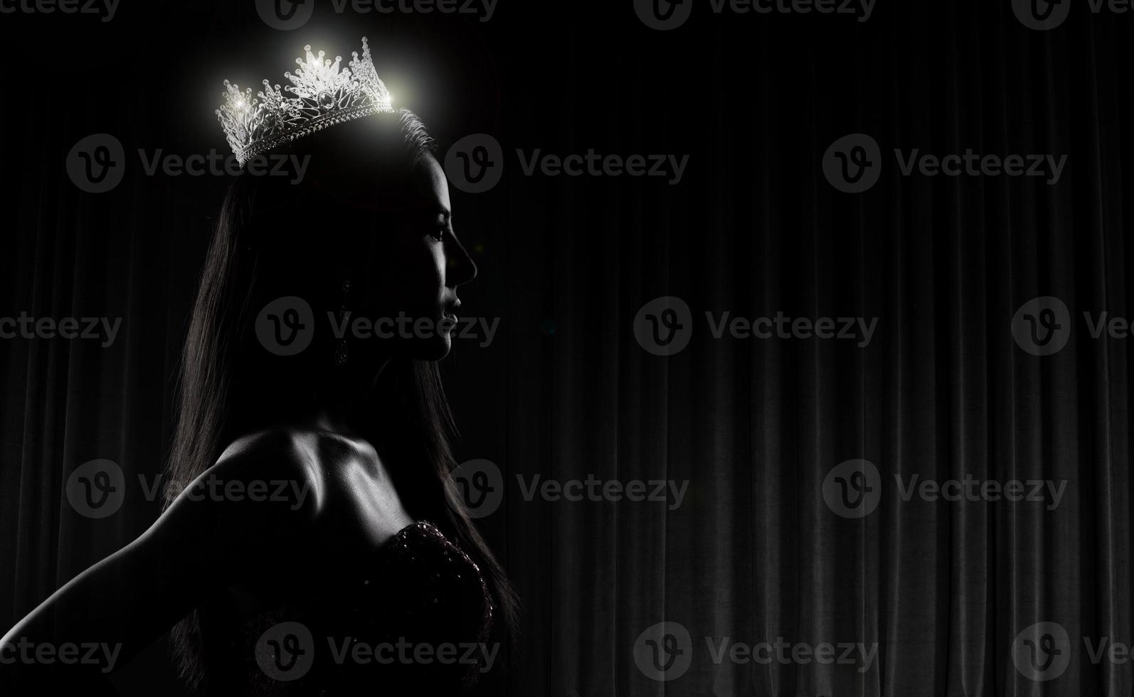 Portrait of Miss Pageant Beauty Contest in sequin Evening Ball Gown long dress with sparkle light Diamond Crown, silhouette low key exposure with curtain, studio lighting dark background dramatic photo