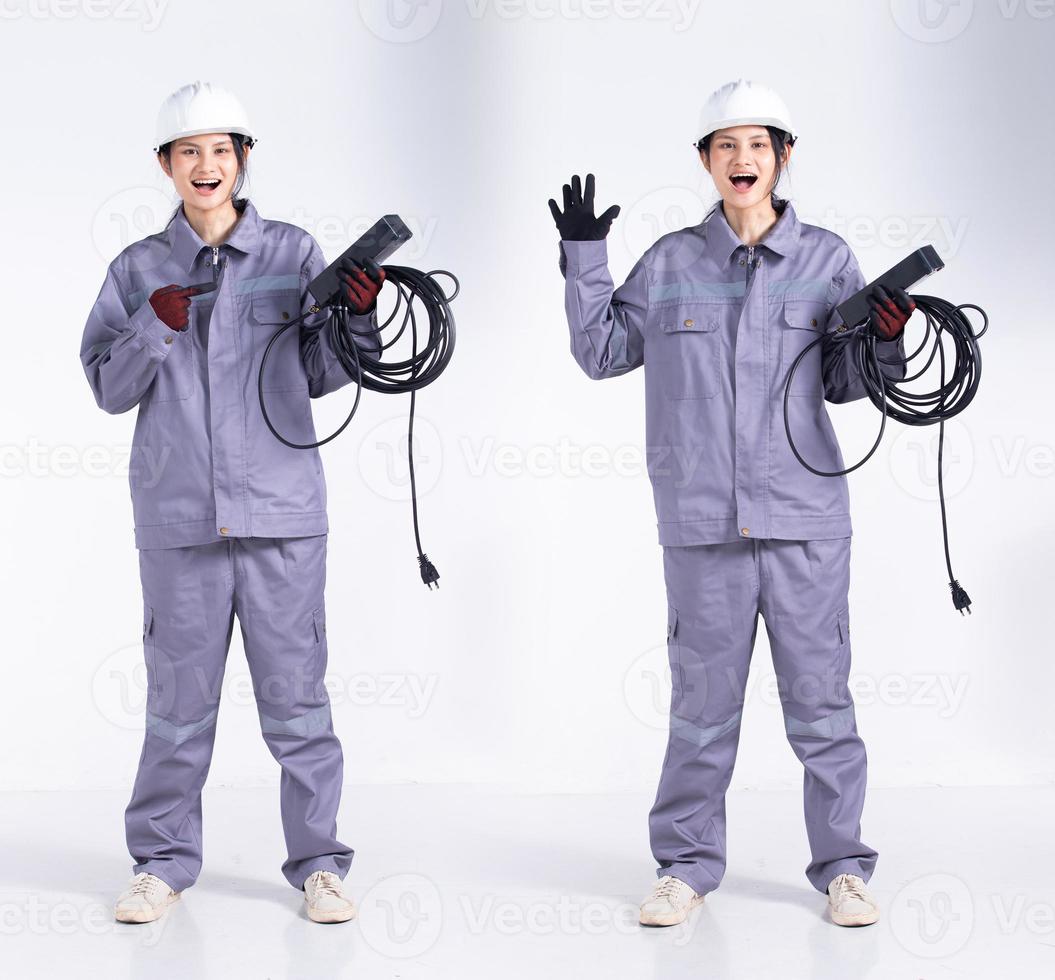 longitud completa 20s joven ingeniero de raza mixta mujer electricista, wow sorpresa signo alegre, usar uniforme gris. Contratista hembra mantenga cable de enchufe eléctrico sonrisa feliz sobre fondo blanco aislado foto