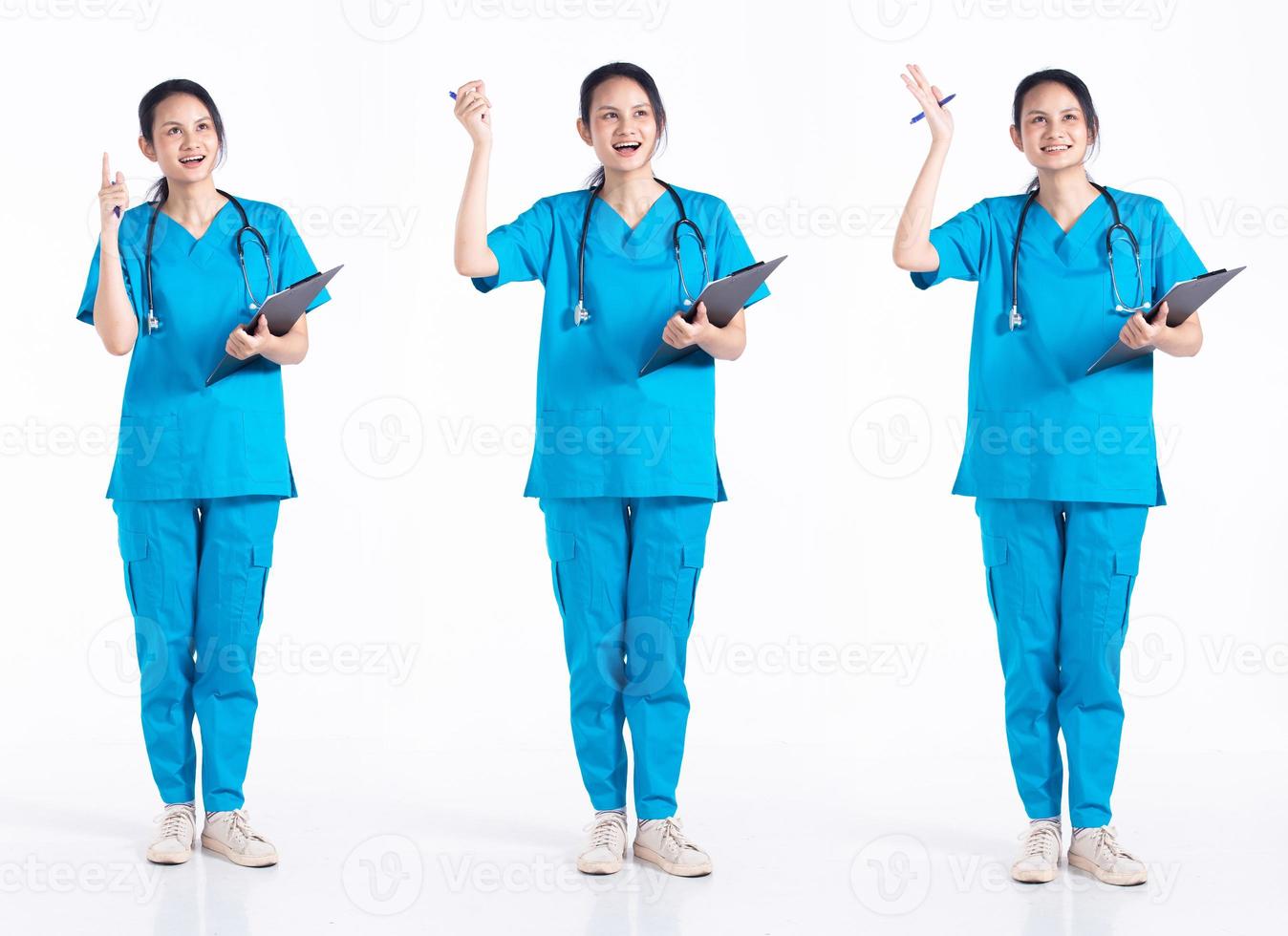 Full length 20s young Mix Race hospital nurse Woman, pointing finger Wow idea, wear stethoscope blue uniform. Doctor female feels smile happy over white background isolated photo