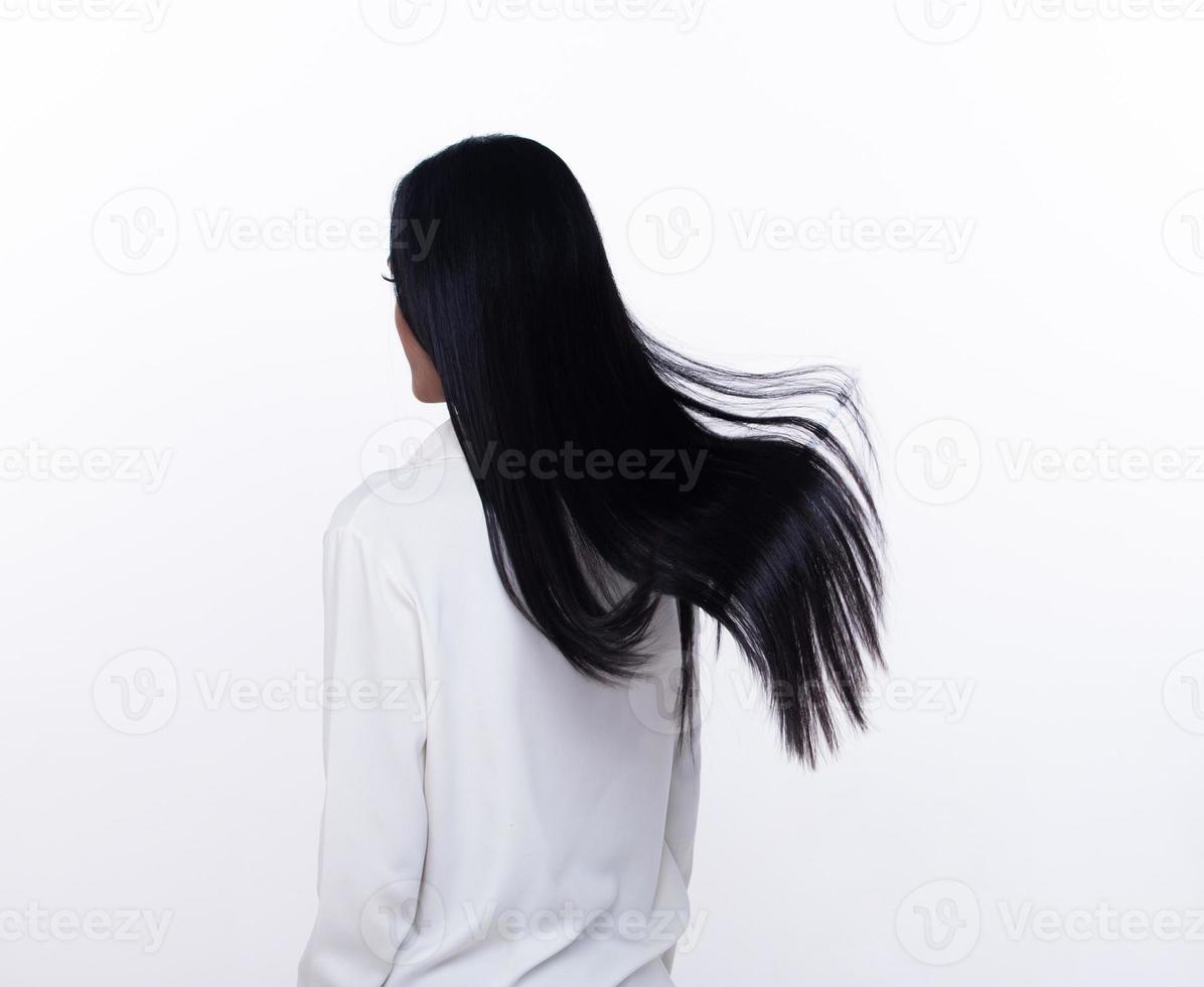 mujer de cabello negro largo y recto negro lanza mosca en el aire con alegría elegante y divertida de moda. hembra vuelta atrás usar camisa blanca expresar emoción feliz por soplar el cabello del viento, fondo blanco aislado foto