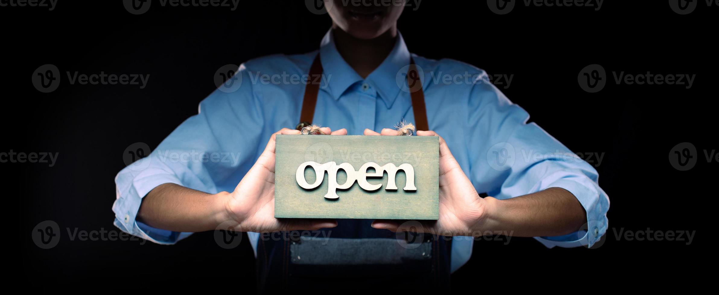 Caucasian person hold Open Sign Business to show service at door entrance store, cafe, retail and welcome shop. Happy Entrepreneur female blonde hair wear waitress dress as open business time concept photo