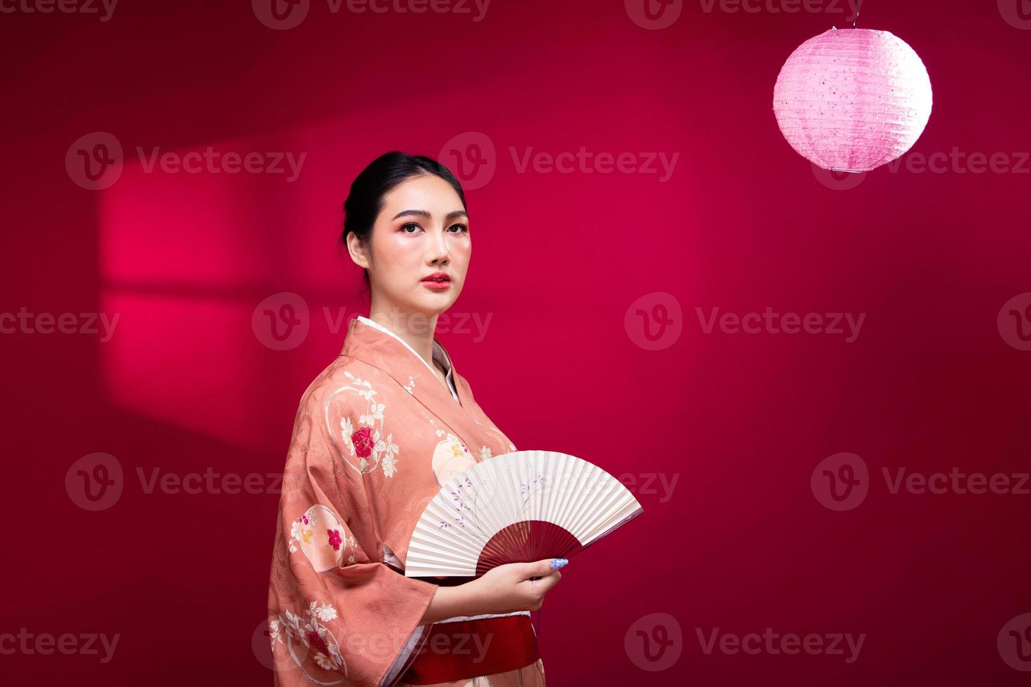 mujer japonesa asiática joven de medio cuerpo de 20 años usa kimono tradicional rosa, sostiene un abanico de arte y una lámpara foto