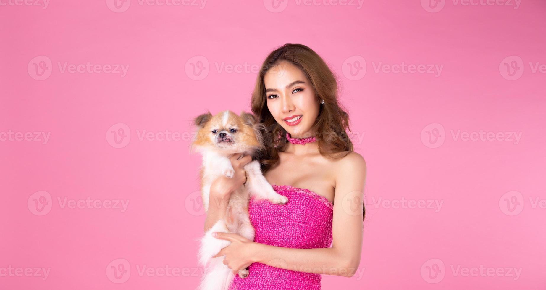 la chica usa un vestido rosa chocky sostiene un perro lindo y mira la cámara sobre un fondo rosa foto