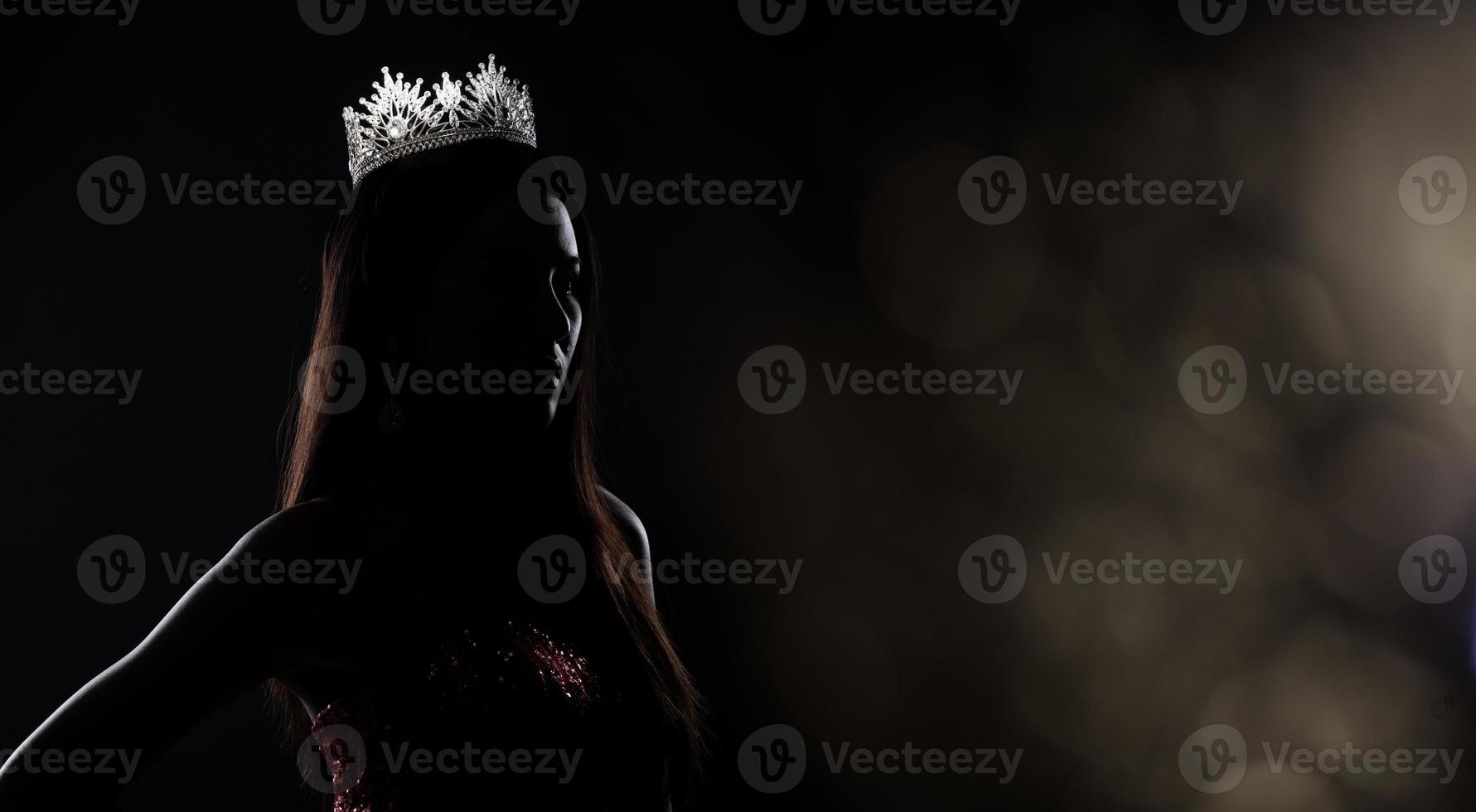 Portrait of Miss Pageant Beauty Contest in sequin Evening Ball Gown long dress with sparkle light Diamond Crown, silhouette low key exposure with curtain, studio lighting dark background dramatic photo
