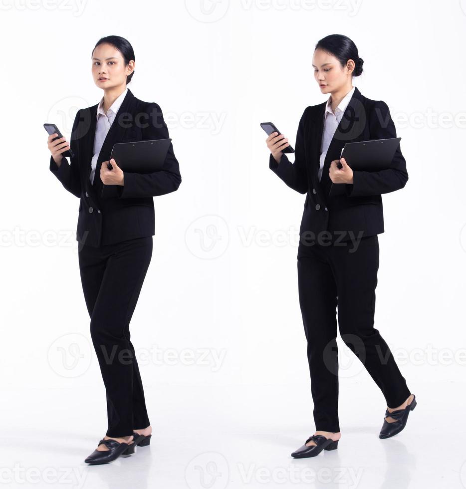 joven mujer caucásica profesora estudiante abogada de 20 años de duración, que usa un teléfono celular inteligente, usa un blazer formal negro y zapatos. Los soportes femeninos de la oficina sienten una sonrisa feliz sobre un fondo blanco aislado foto
