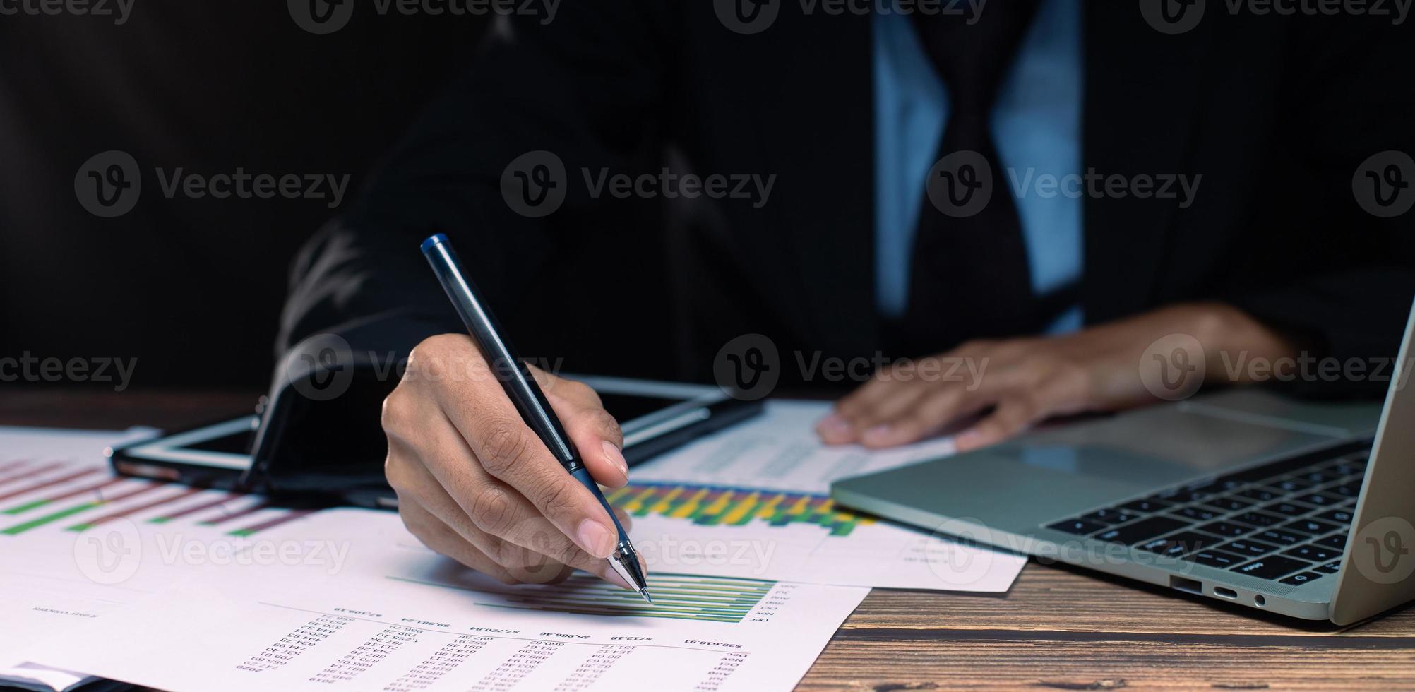 Businessman executive manager hand point pen to paper business document, graph sales growth, partnership agreement and working on desk in night time at office, close up photo