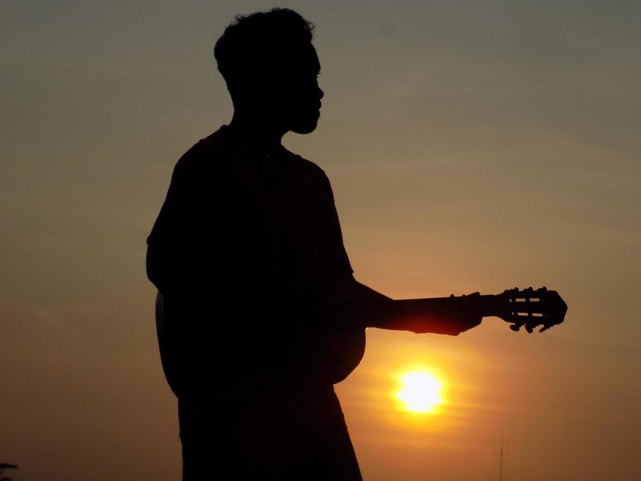 silhouette of a person playing guitar on a sunset background photo
