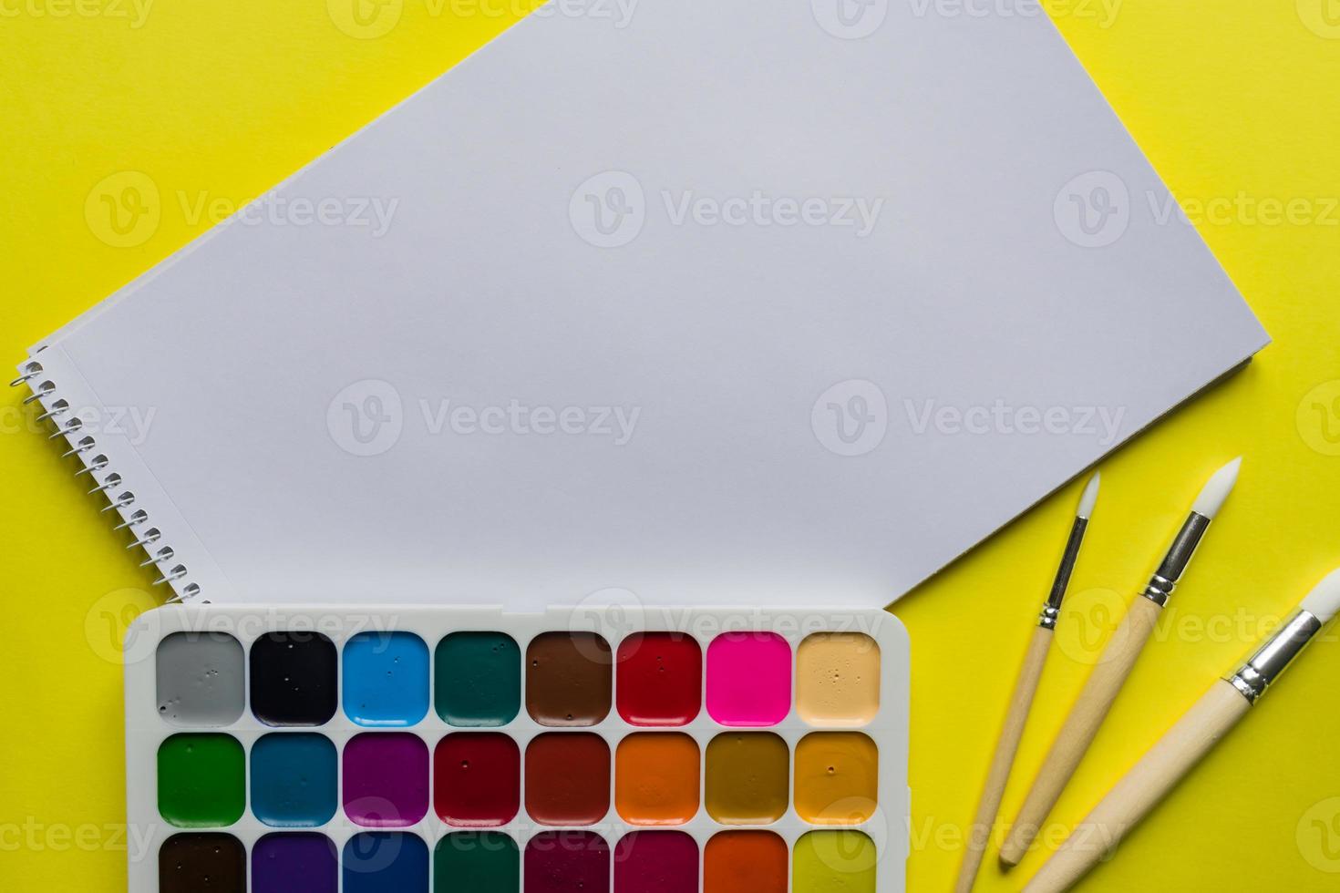 Creative layout with aquarelle palette, paint brushes and sketchbook on yellow background. Copy space for text. photo