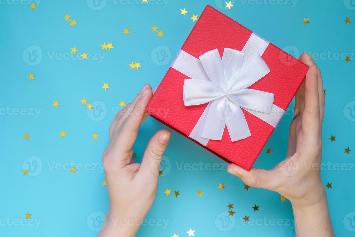 mujer abriendo caja de regalo roja sobre fondo de color azul. tarjeta de felicitación festiva. concepto de vacaciones. foto