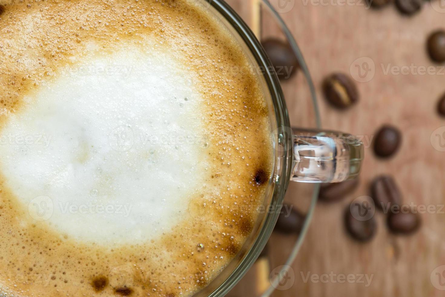 Top view of cup of hot latte or cappuccino in a glass cup on wooden table. Coffee with milk foam with copy space photo