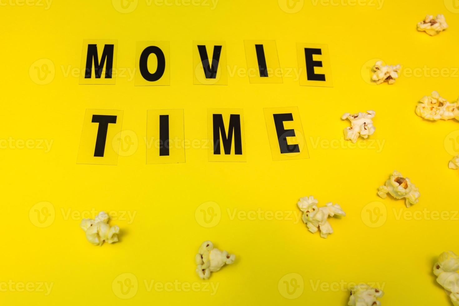 popcorn and text movie time on yellow paper background. Concept of cinema and entertainment. Flat lay photo