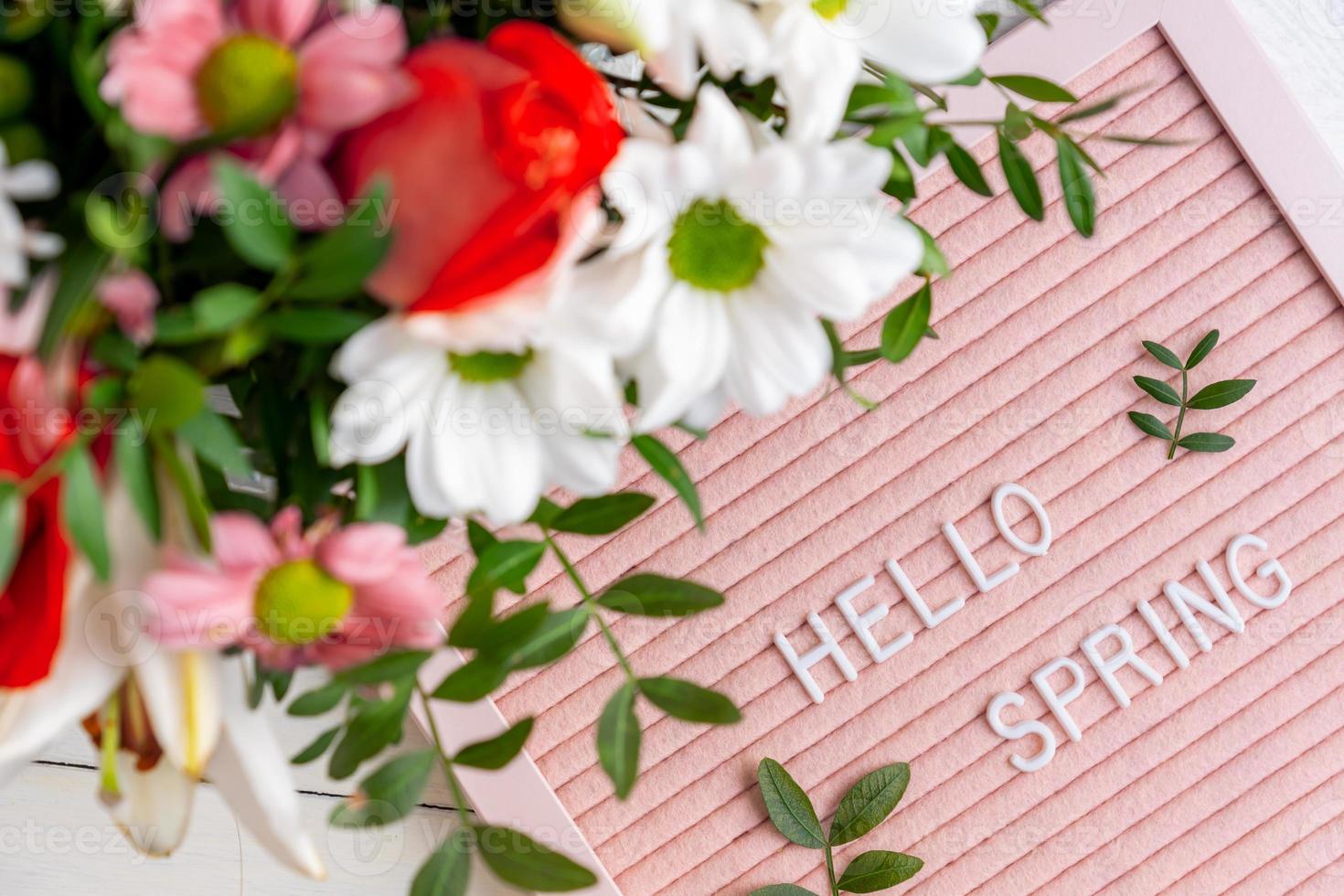 Text Hello Spring on pink letter board and bouquet of colored flowers. Concept Springtime mood and happiness. photo