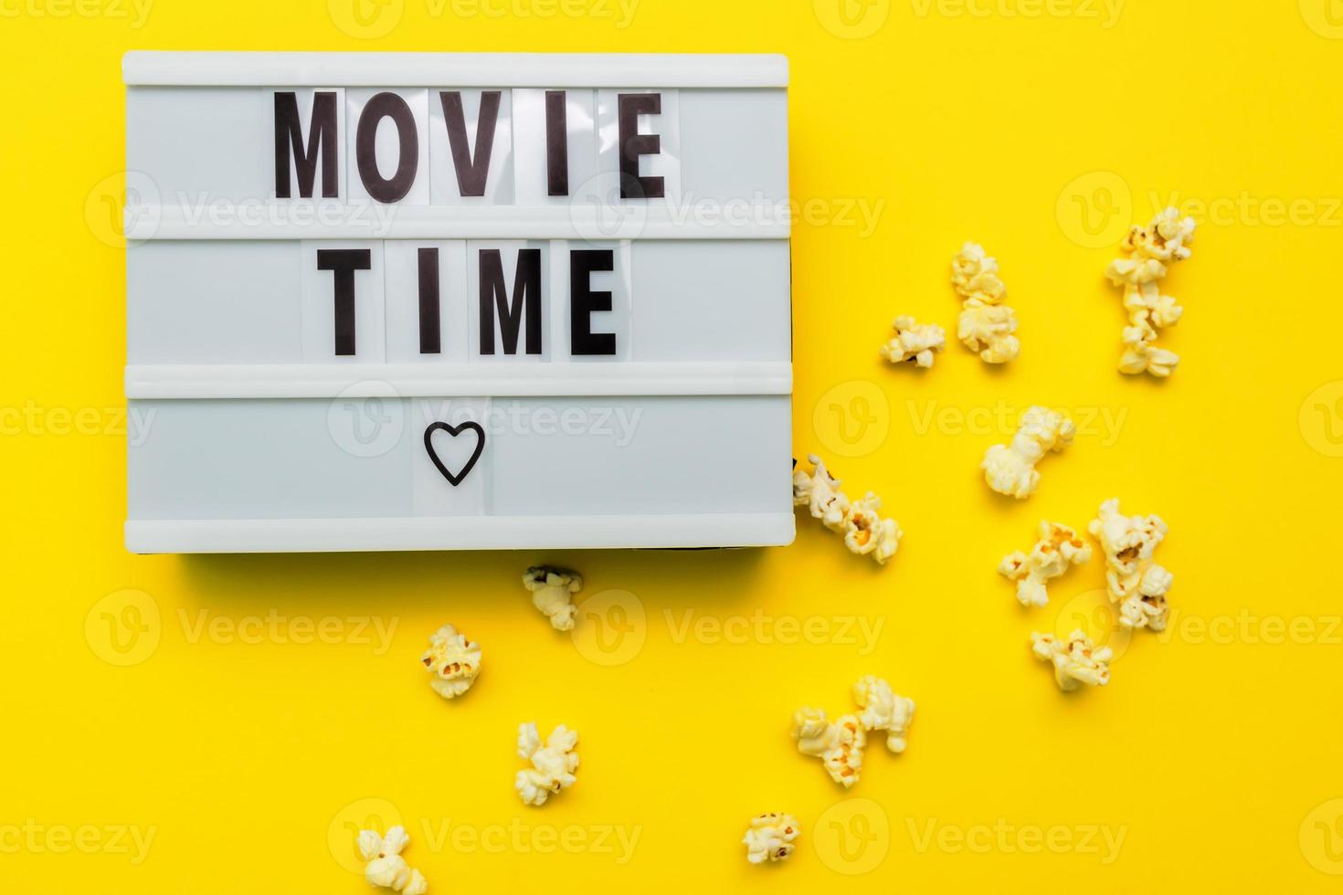 Movie Time text on a light box. Scattered salty popconn on yellow background photo