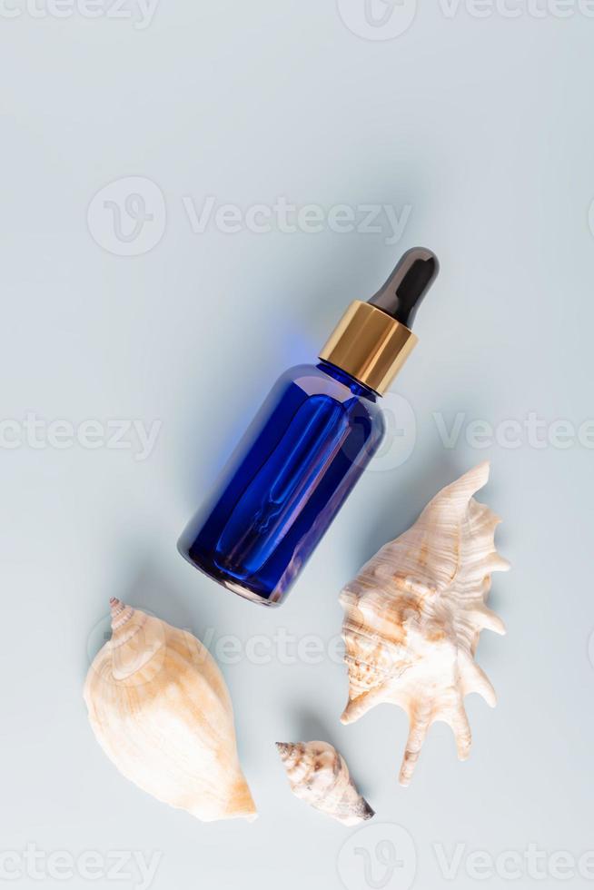 Blue glass cosmetic bottle with pipette, seashels on blye background. Natural organic cosmetics for face and body, aroma oil. Beauty concept. Products for branding, mock up photo