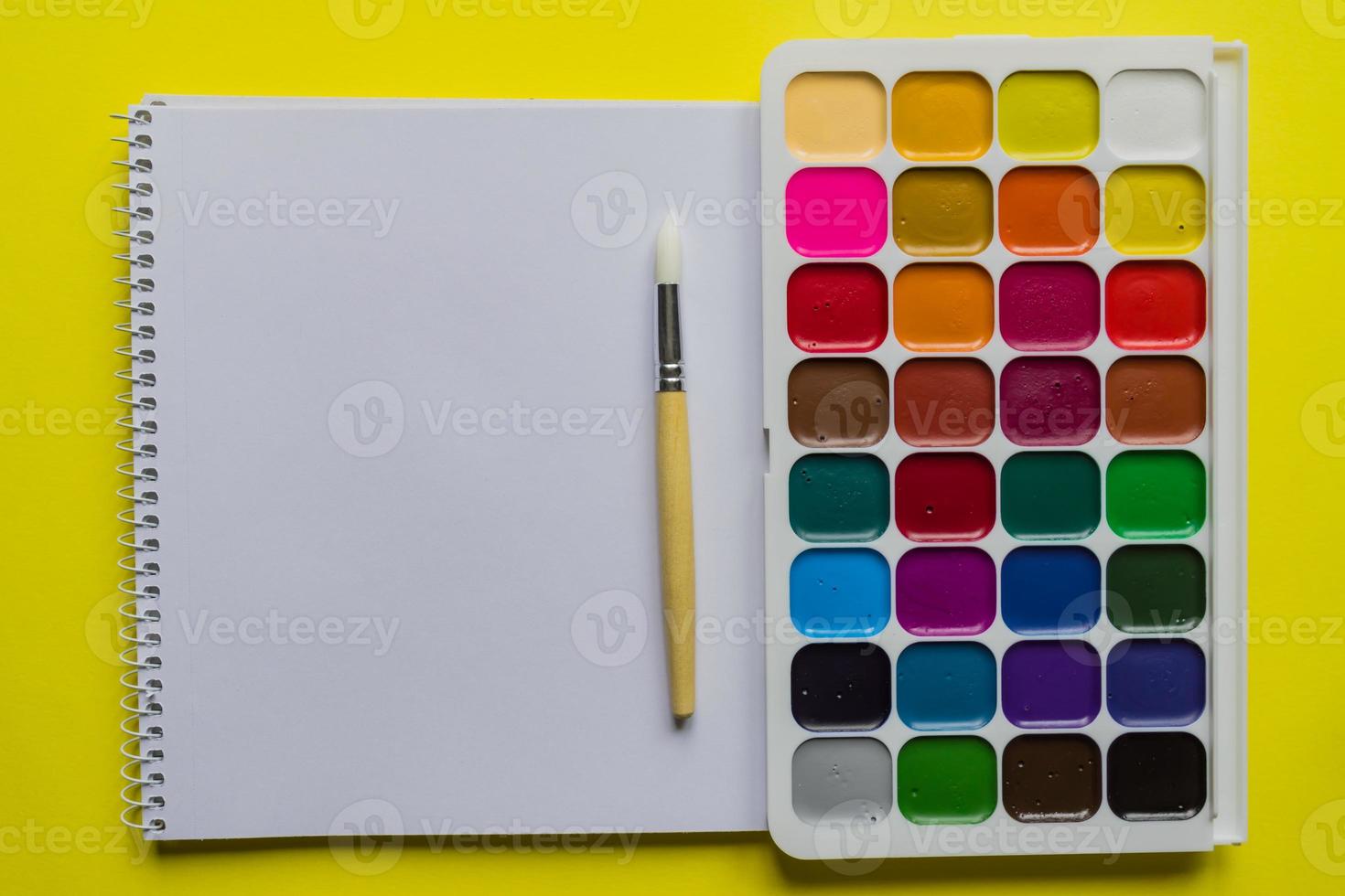 Watercolor paints and brushes on yellow background, top view. Creative artistic mockup with copyspace. Aquarelle painting photo