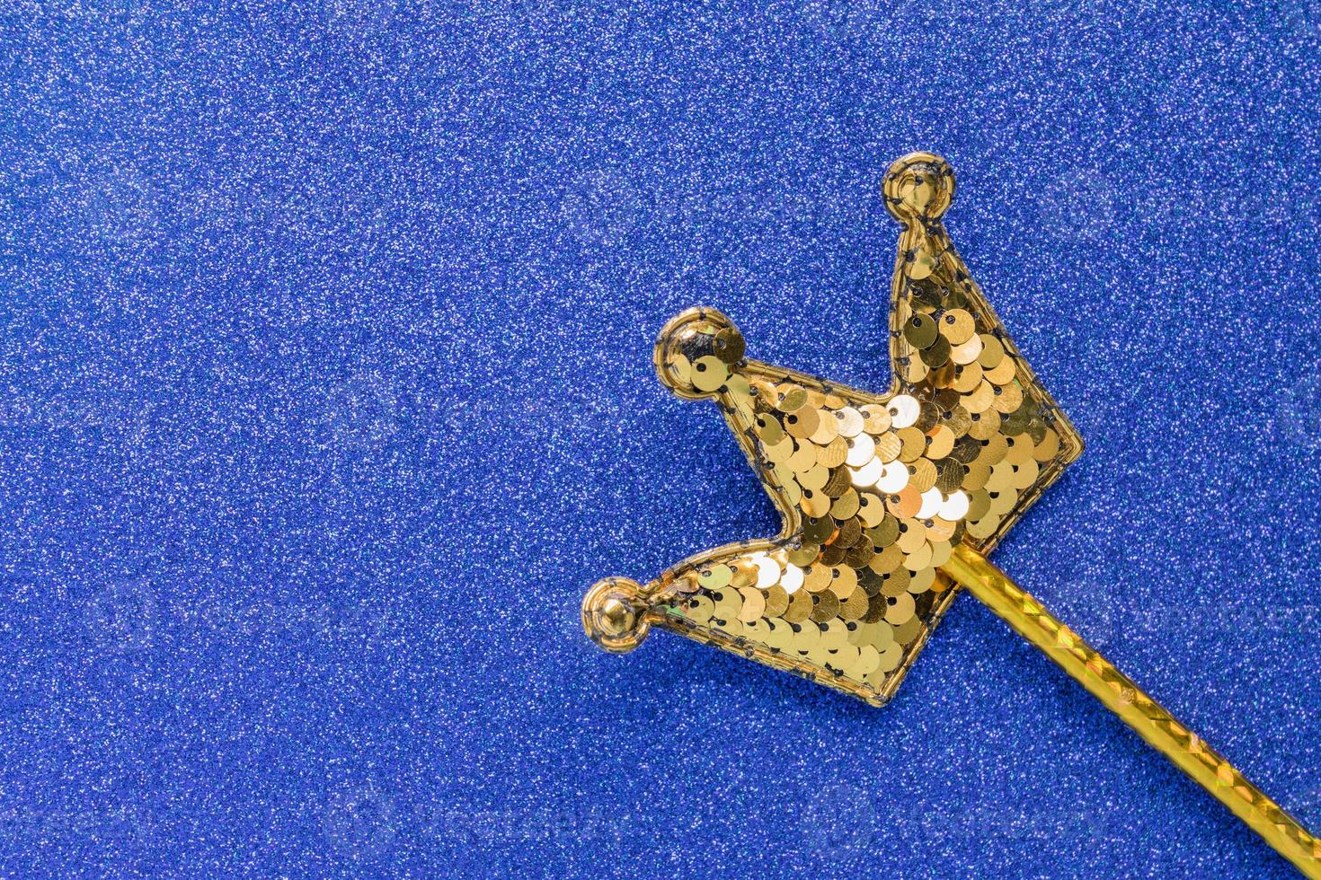 palo mágico dorado de lentejuelas en forma de corona sobre fondo de brillo azul. primer plano creativo foto