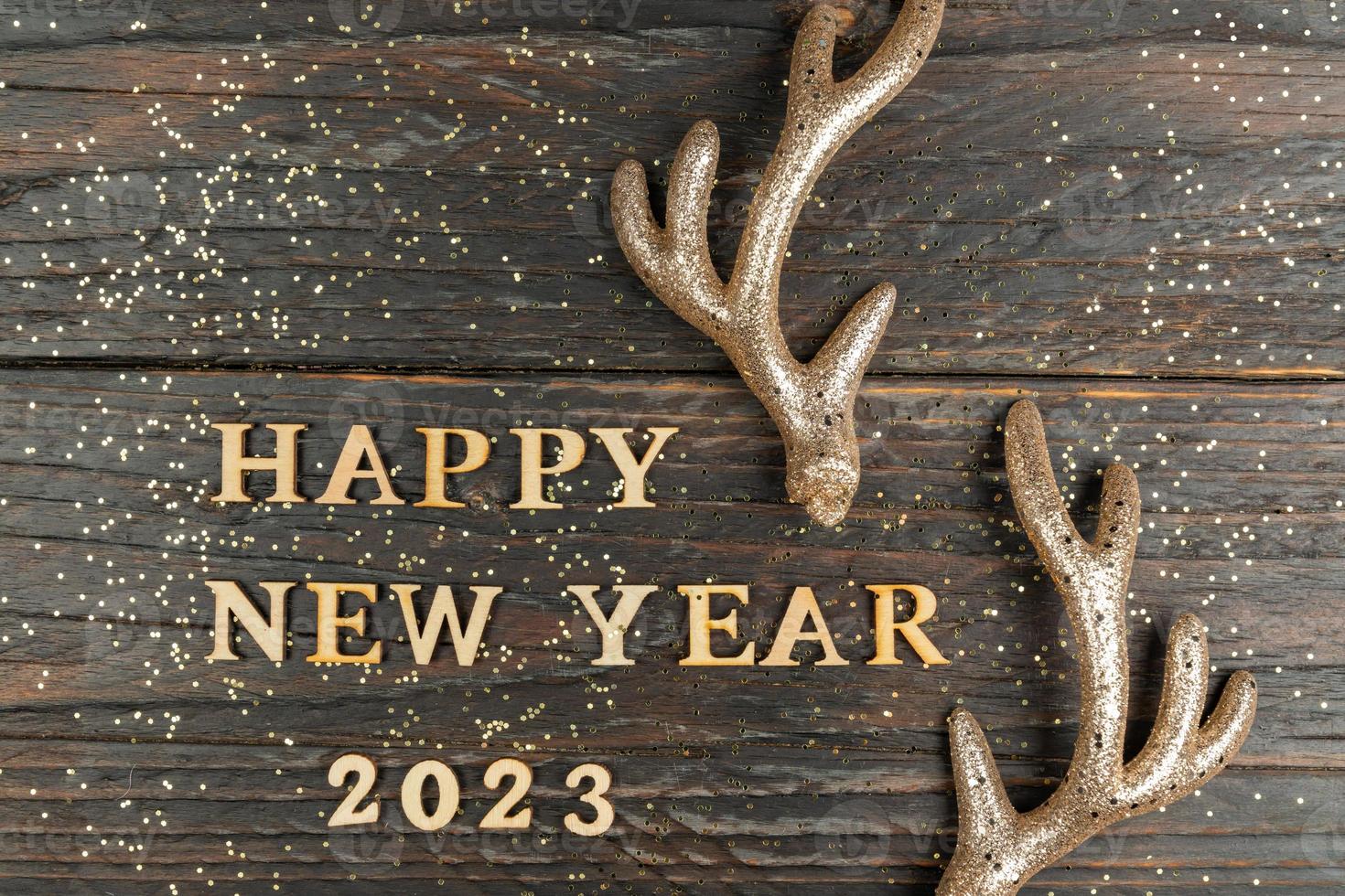 Happy New Year 2023. Quote made from wooden letters and numbers 2023 on wooden background decorated raindeer horns. Creative concept for new year greeting card photo
