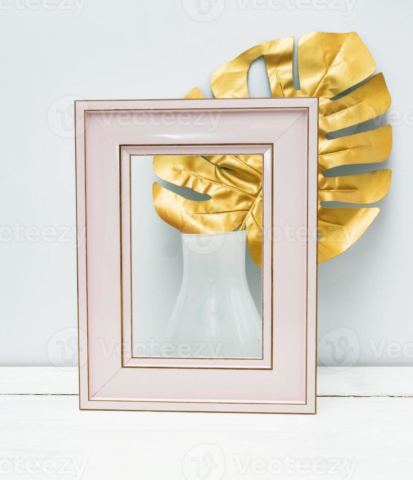 interior design. Empty pink photoframe and monstera leaf in white vase on white wall background. Trendy luxury design. Copy space for text. photo