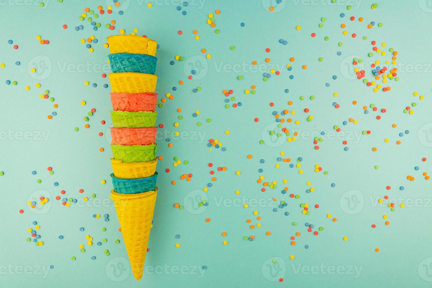 Set of various bright multicolored ice-cream waffle cones on blue background with scattered confetti sugar sprinkles. photo