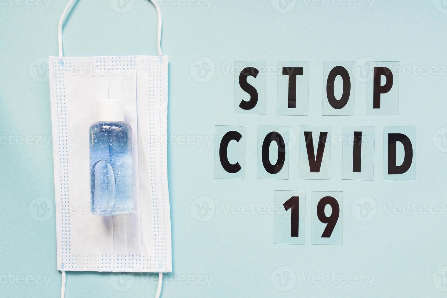 medical mask and sanitizer on blue background and text stop covid 19. hygienic quarantine concept. Flat lay, top view photo