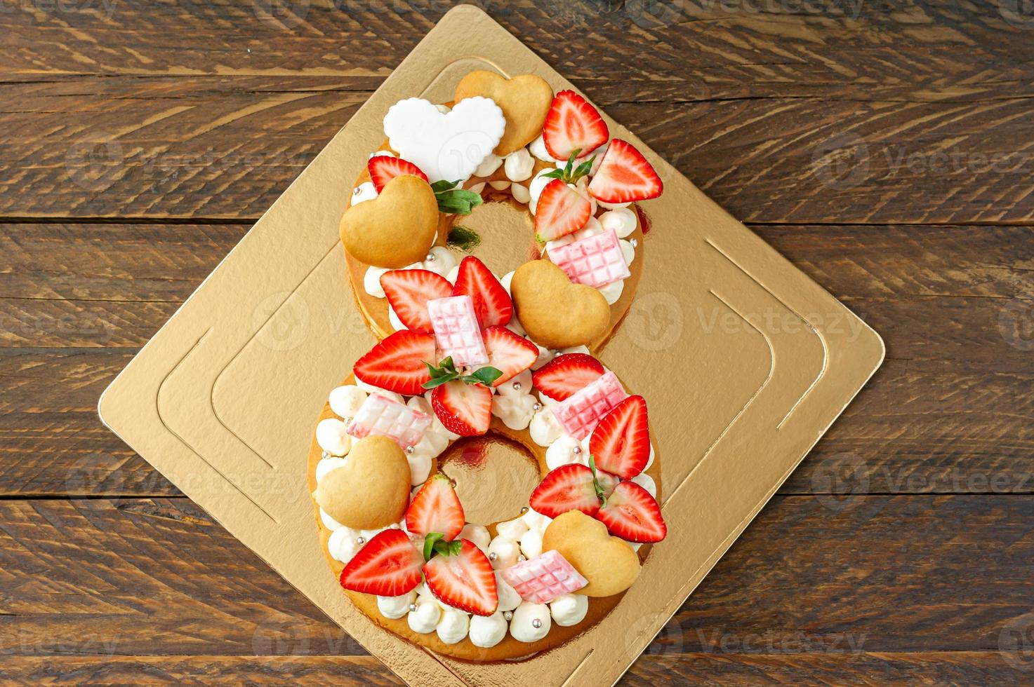 Sponge cake with strawberries, pink milk chocolate bars, silver sprinkles, vanilla cream and heart chape cookies in shape of number 8. Spring sweet dessert for international woman day. Sweet present photo