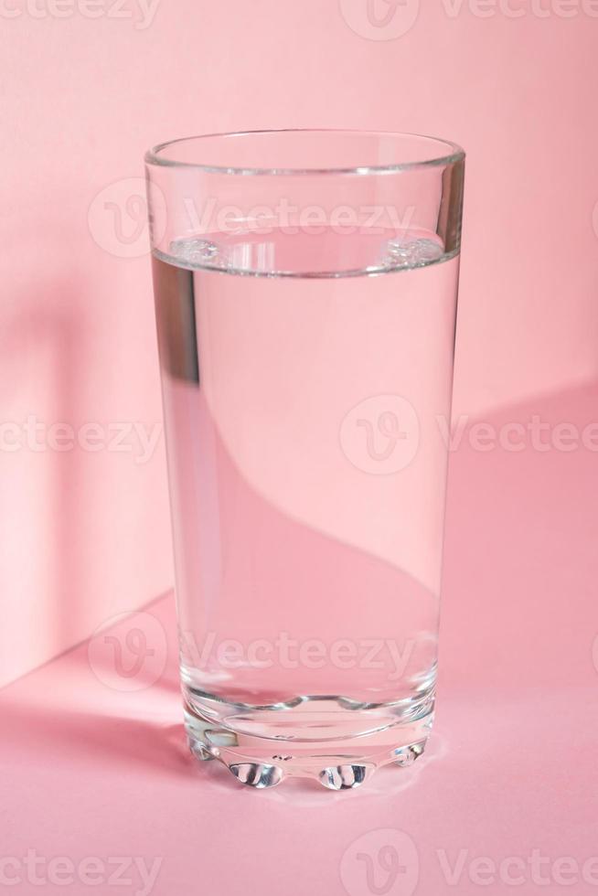 Close up of sparkling water in transparent high glass and sun glare on pink background photo