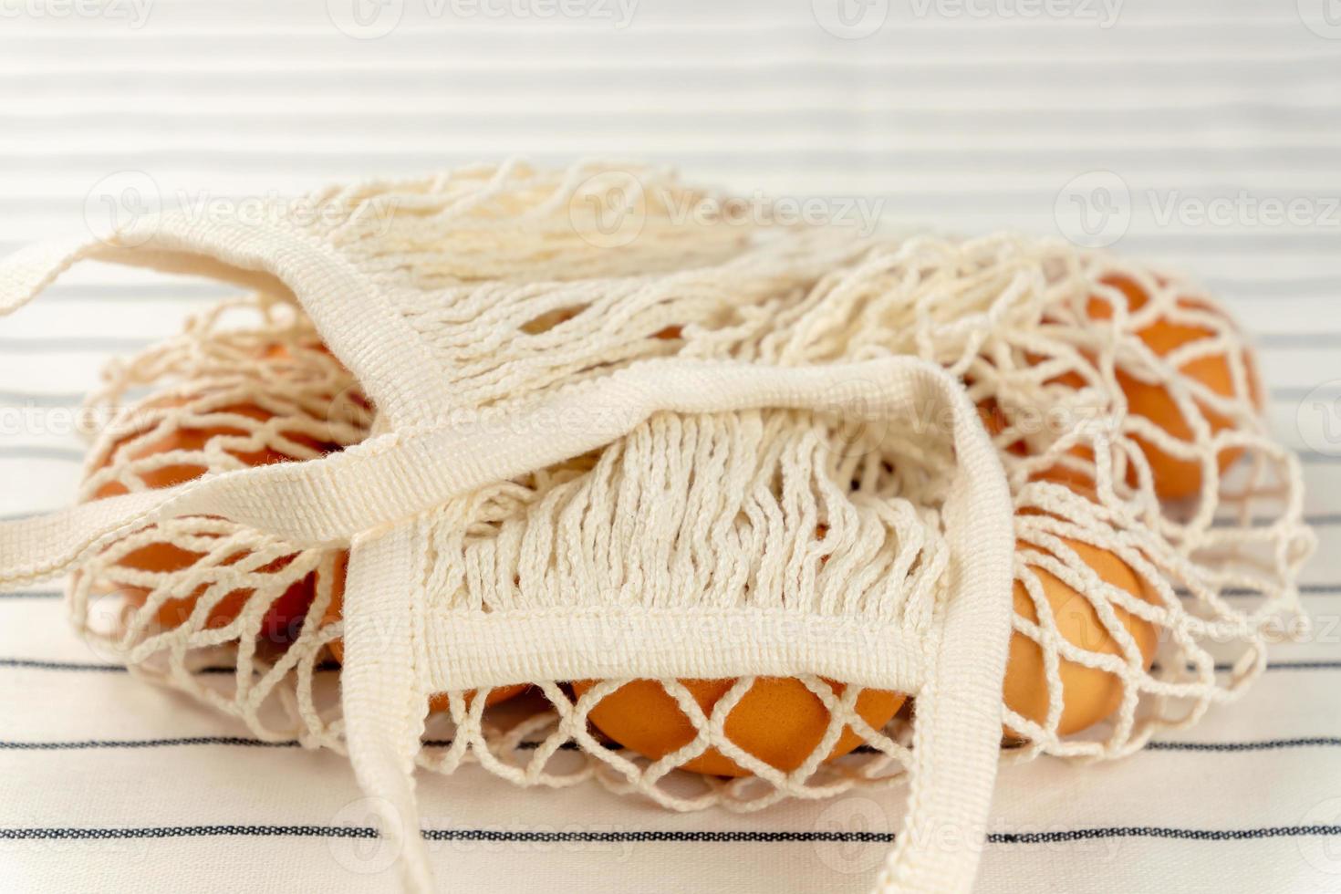 Easter concept. No plastic bag concept. Minimal style. Beige mesh shopping bag with brown chicken eggs on textile background. photo