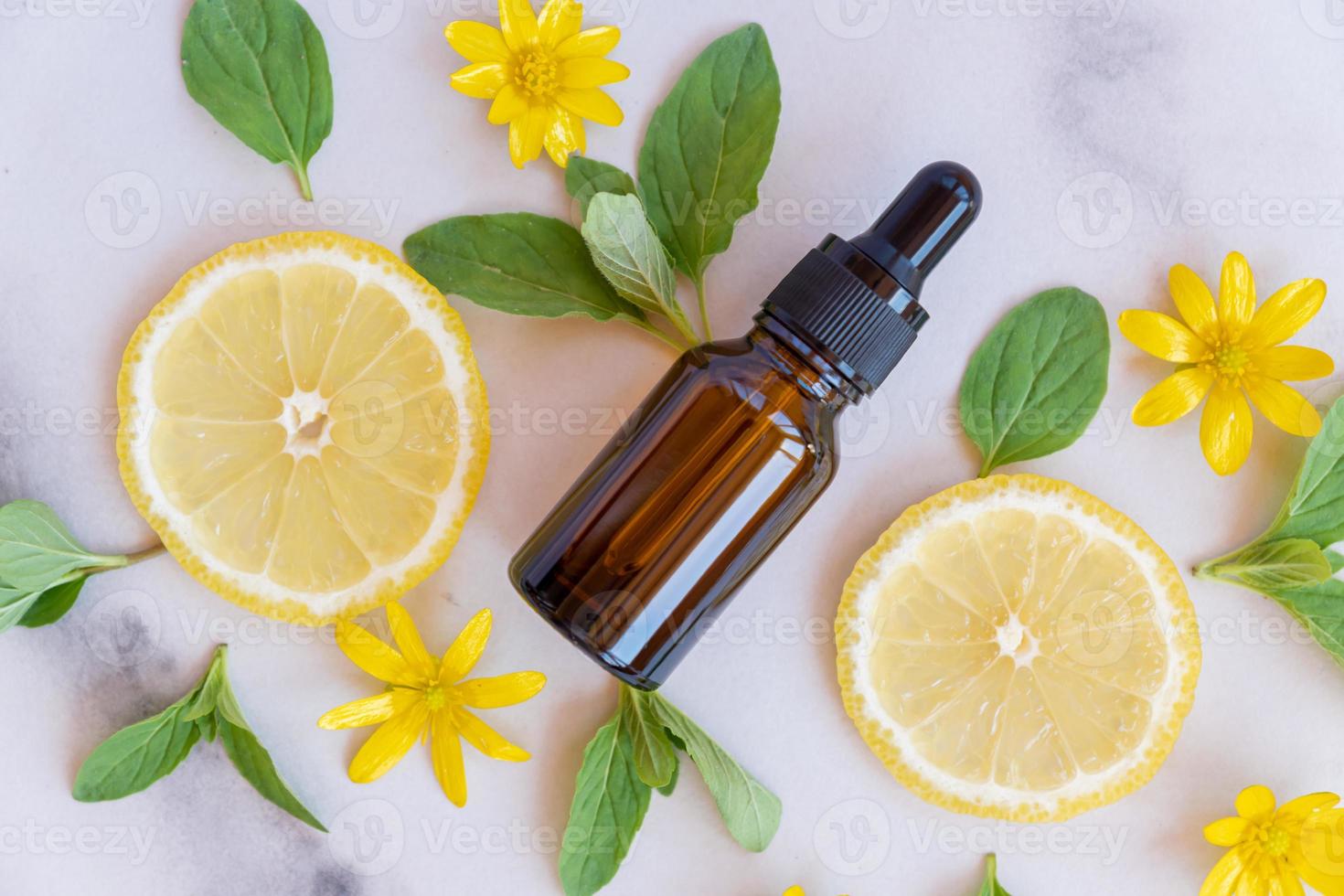 Serum with vitamin C. Lemon essential oil. Brown glass bottle with a pipette, slices of lemon with mint leaves on a marble background. Health and beauty concept. Organic Natural Cosmetics photo