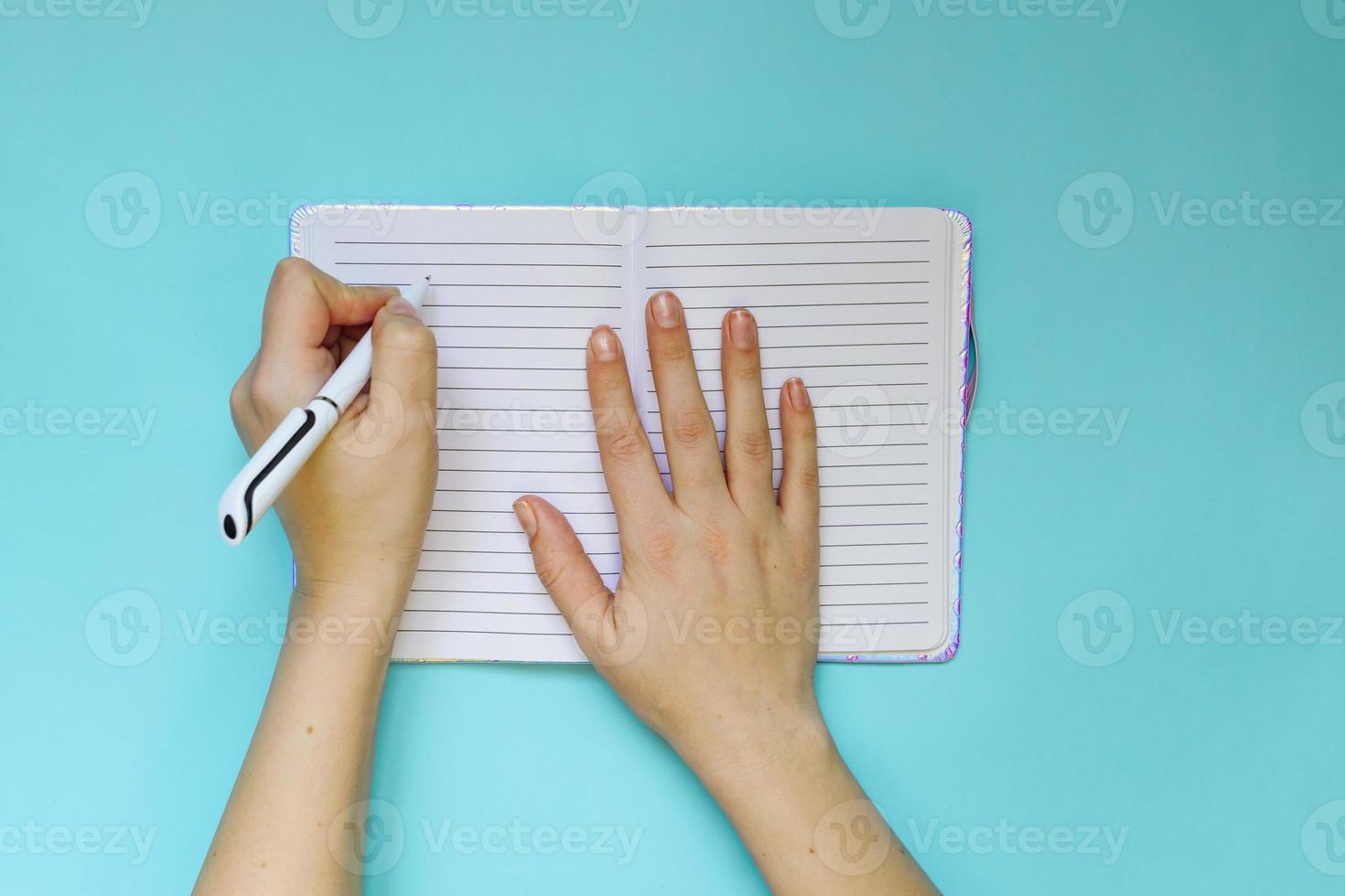 Left handed woman makes notes in her planning or dary on blue background. Planning concept. Flat lay style. photo